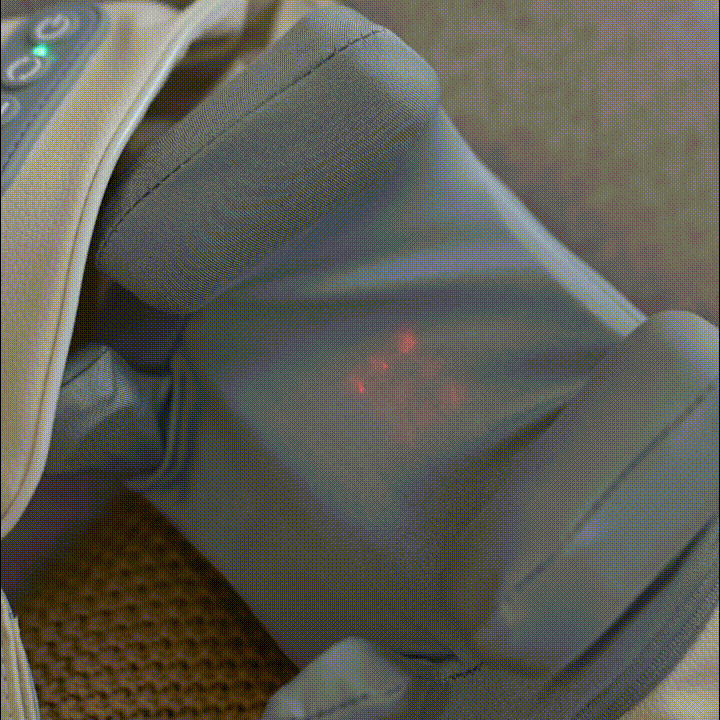 Gråt massageapparat med røde LED-lys, placeret på en brun overflade, velegnet til muskelafspænding.