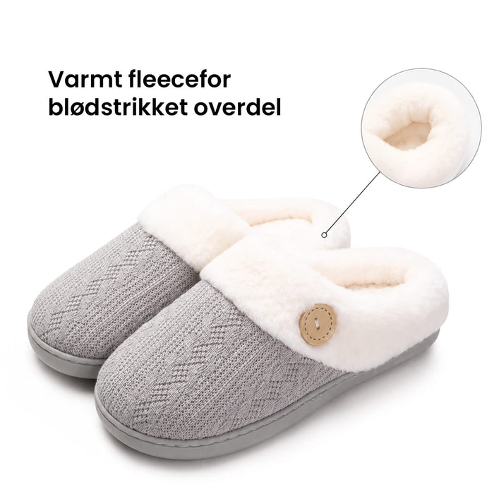 Grå hjemmesko med hvidt fleecefor, skridsikker sål, knap i siden og cirkulær detalje.