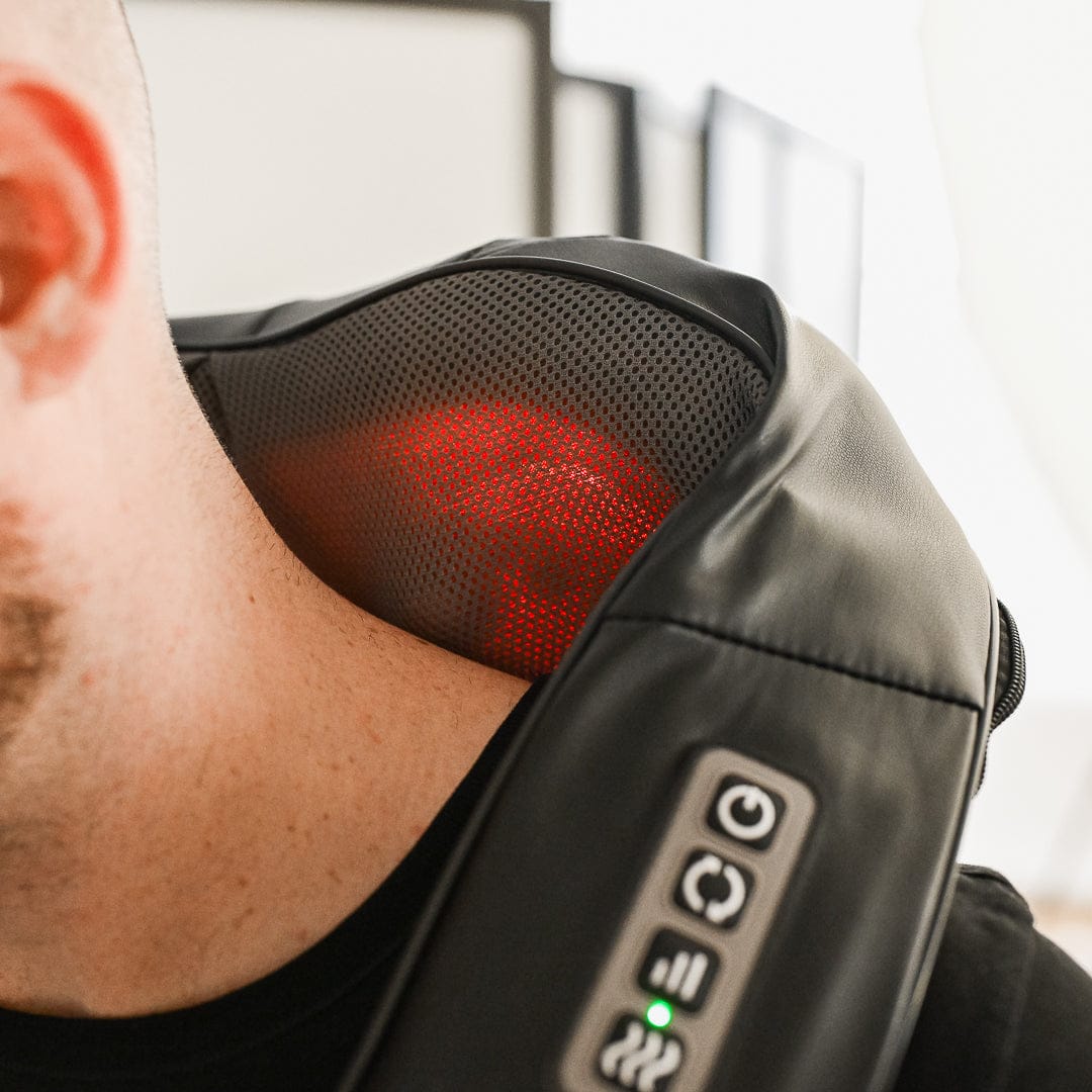 En person har en sort nakkemassager med betjeningsknapper, synligt rødt lys og et ergonomisk design på skulderen.