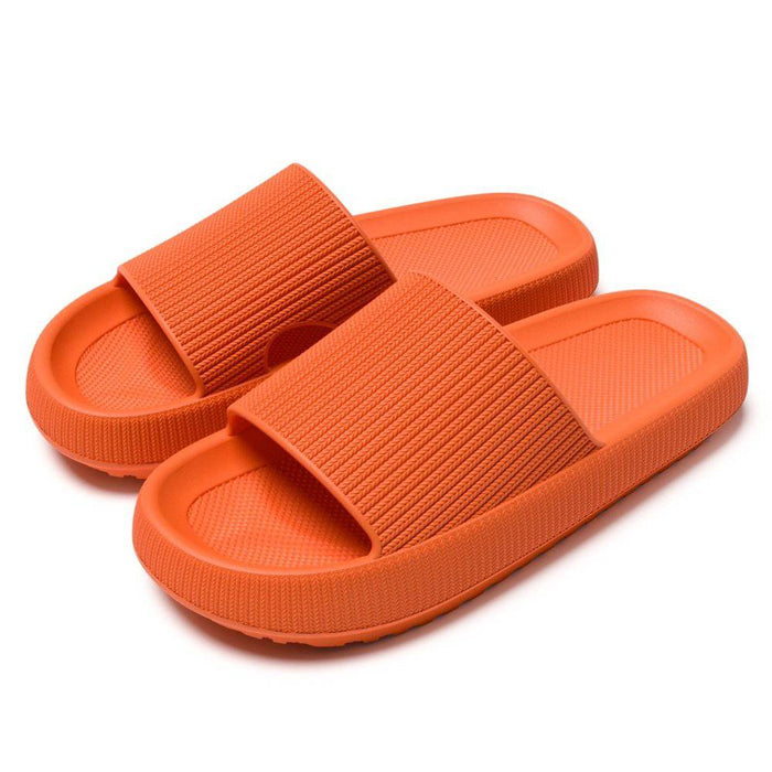 Stødabsorberende orange hjemmesko med brede remme og sål af memory foam, vist på hvid baggrund.